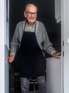 An elderly gentleman is standing in a doorway, wearing a smile.