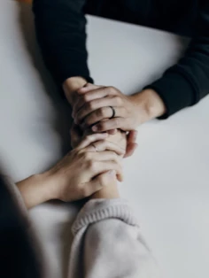 Two individuals are holding hands while sitting at a table.